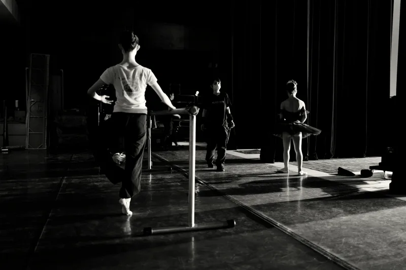 Dancers rehearsing at the barre on a dark studio stage.