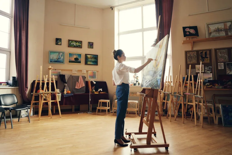 A person setting up easels in a bright art studio.