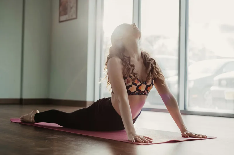 A person in an upward-facing dog pose on a mat beside a bright window.